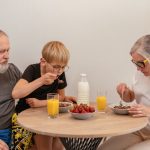 A family of three enjoying breakfast around a wooden table at home.